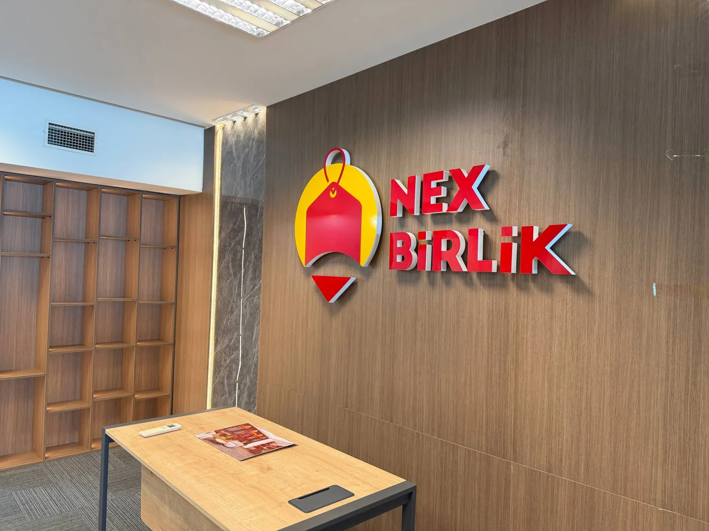 Taxta divarda brend nişanı və qarşısında masa