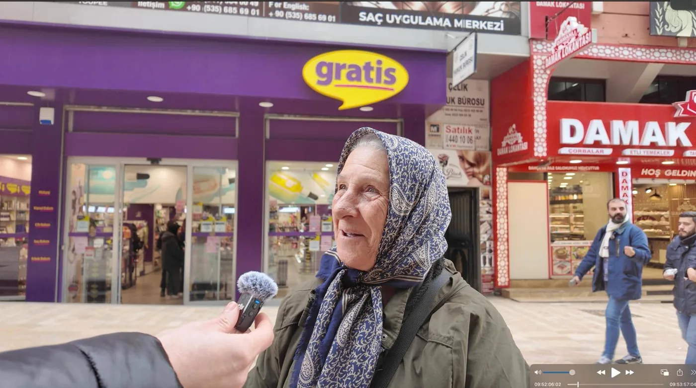 Mağaza qarşısında mikrofonla danışan yaşlı qadın; alıcı rəyi kimi təqdim edilmir · müştərinin təqdim etdiyi foto